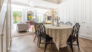 A dining room with a round table, black chairs, and a patterned tablecloth. There is a bookshelf with books and a mirror in the background. - Brunswick Gardens II by Onefinestay (London)