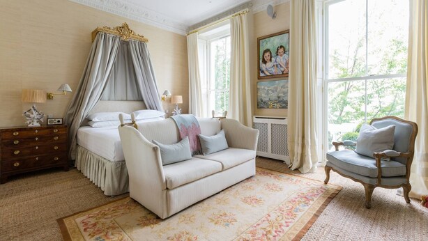 A bedroom with a bed, a sofa, a chair, a nightstand, and a large window with curtains. - Brunswick Gardens II by Onefinestay (London)