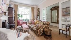 A spacious living room with a fireplace, a large window, and a floral-patterned sofa. - Brunswick Gardens II by Onefinestay (London)
