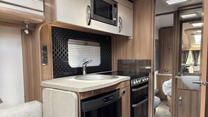 A compact kitchen with a sink, stove, and microwave. - 4 Guests - Pet Friendly - Durham Caravan Retreat (Durham)