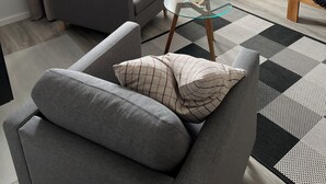 En moderne stue med en grå sofa, et glasbord, et tv-møbel i træ og udsigt ud af vinduet.