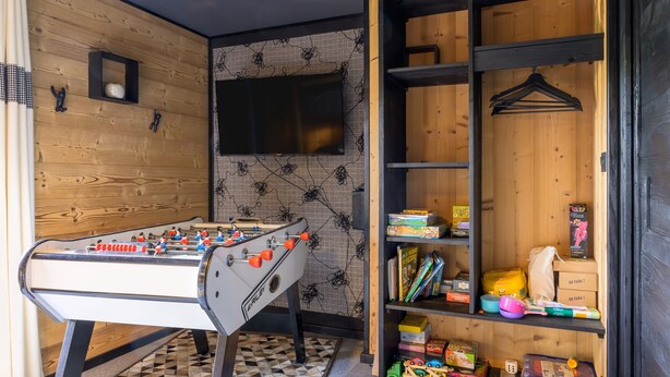 Ein Zimmer mit Kicker, Fernseher und einem Regal voller Kinderspielzeug und Bücher.