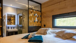 A modern bedroom with a large bed, a wooden wall panel, a window, and a bathroom with a mirror and sink.