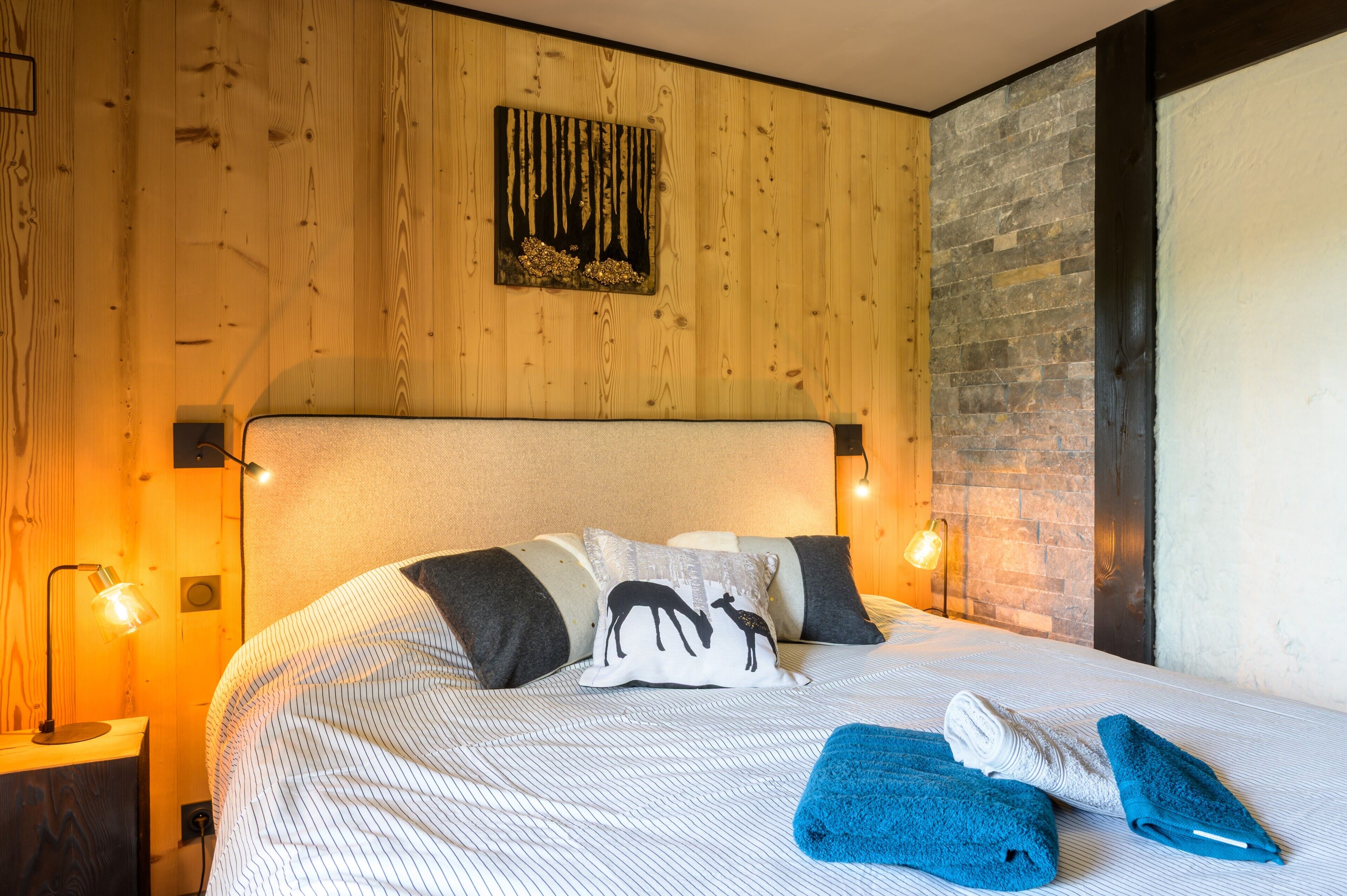 A neatly made bed with striped bedding, a headboard, and two bedside lamps.