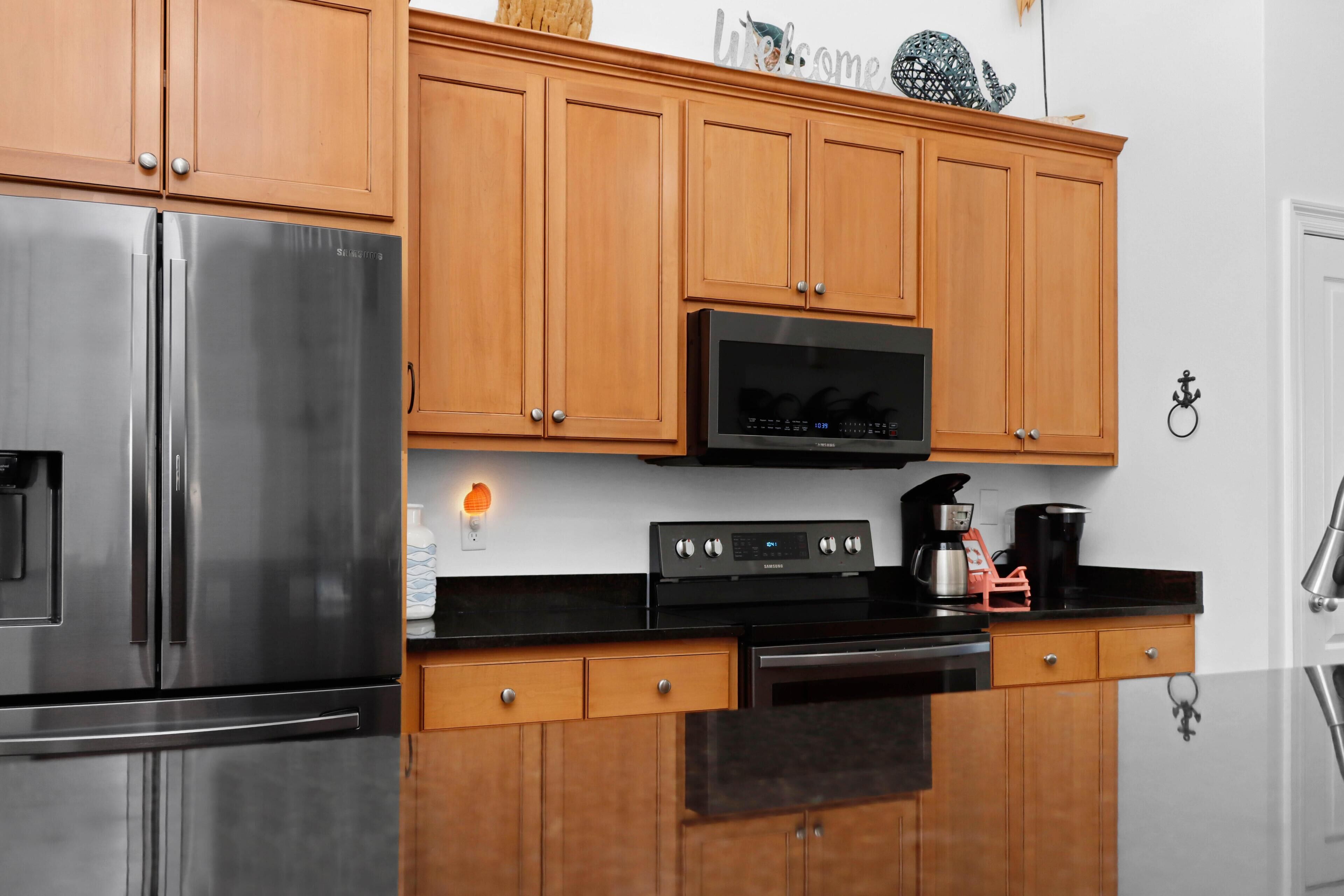 A modern kitchen with wooden cabinets, stainless steel appliances, and a black microwave.