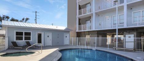 A pool area with a small building, lounge chairs, and a multi-story building with balconies.