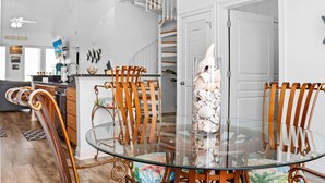 A dining area with a glass table surrounded by wooden chairs, a decorative shell centerpiece, and a staircase in the background. - Tranquil Harbor 311 - Sea Forever (Port St. Joe)