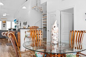 A dining area with a glass table surrounded by wooden chairs, a decorative shell centerpiece, and a staircase in the background.