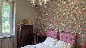 A bedroom with a floral wallpaper, a wooden dresser, a bed with pink headboards, and a chandelier. - Family home in green setting near village, municipal swimming pool, nogaro (Panjas)
