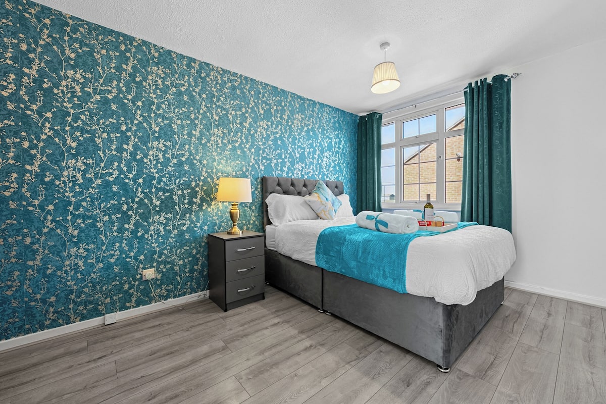 A bedroom with a bed, a nightstand, a lamp, and a window with curtains.