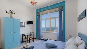 Un dormitorio con cama, escritorio, silla, armario, ventana con vistas y televisor en la pared.