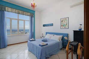 A bedroom with a bed, a view of the sea, a desk, and a chair.