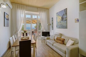 A living room with a sofa, TV, dining table, chairs, and a painting.