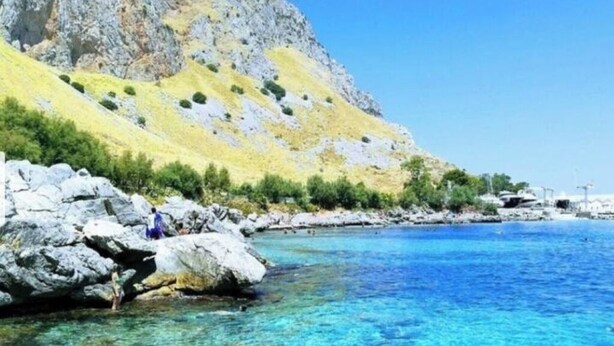 Un paysage côtier avec une eau bleue et limpide, une côte rocheuse et une montagne en arrière-plan.