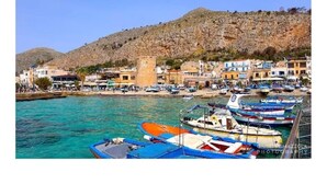Une ville côtière avec une colline rocheuse, une tour et des bateaux amarrés dans le port.