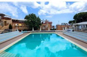 Una piscina con escalones de acceso, rodeada de edificios y árboles.