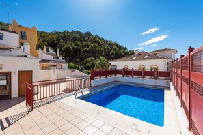 Una piscina con una cerca roja, un deck de baldosas y edificios al fondo.