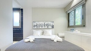 A modern hotel room with a large bed, a cityscape artwork above the bed, a window with blinds, and a white bathroom with a towel rack. - Villa Hamo - 6 rooms (Cannes)