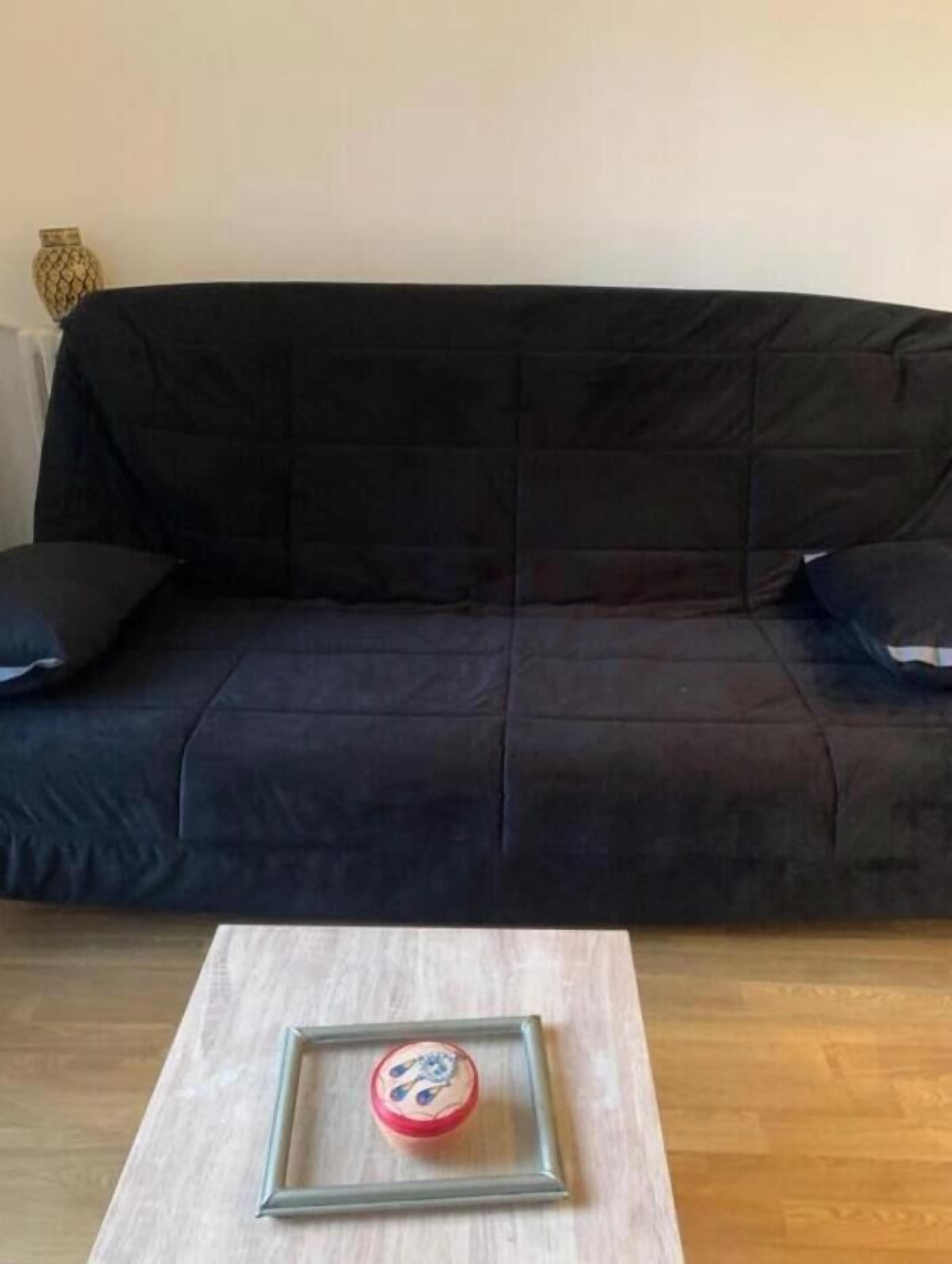A living room with a black sofa, two black cushions, and a small table with a framed object on it.