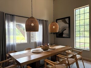 Un comedor con mesa de madera, lámparas colgantes de fibras tejidas y un amplio ventanal con vista a la vegetación.