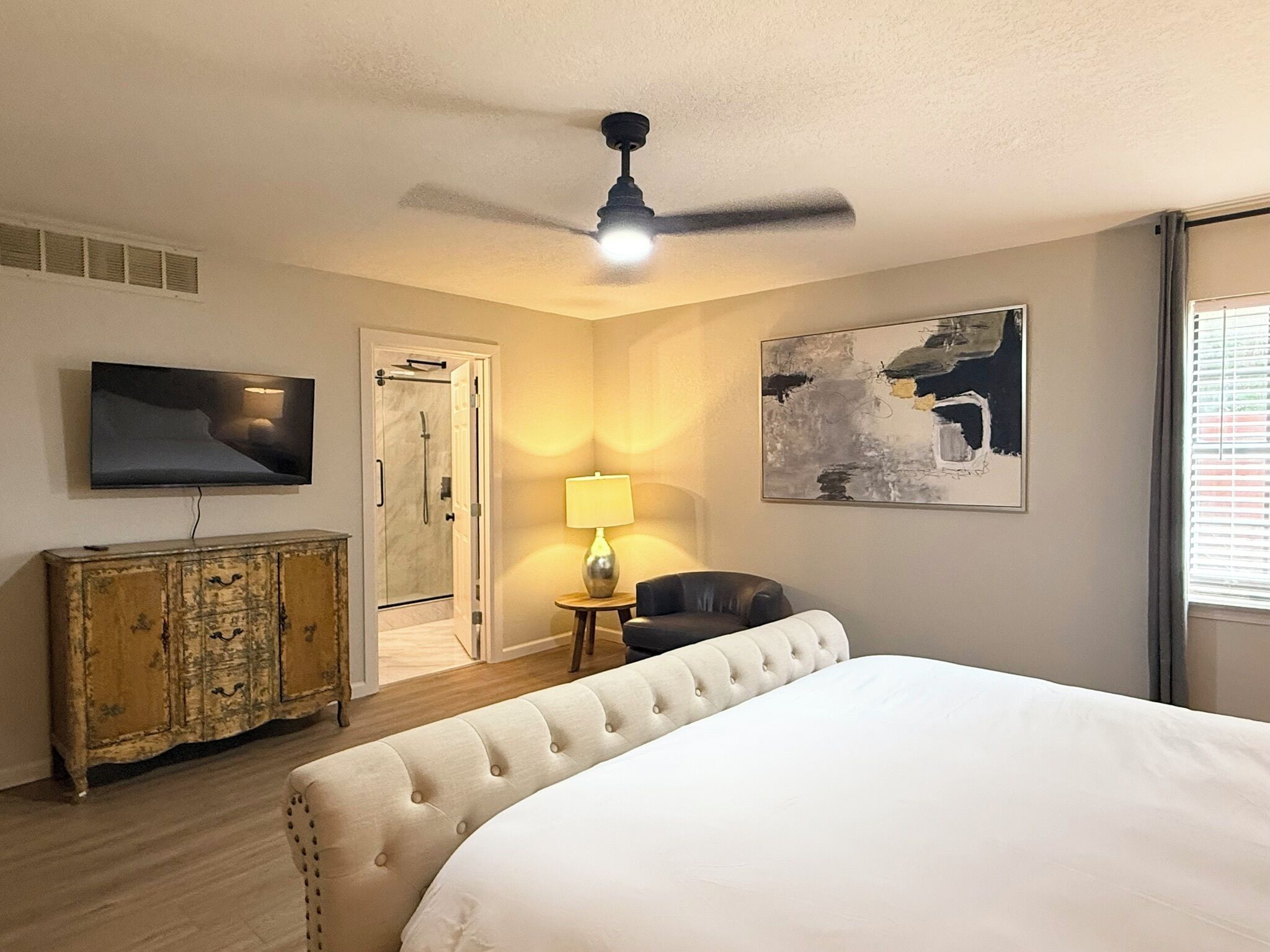 Une chambre d’hôtel équipée d’un lit, d’une télévision, d’un ventilateur de plafond, d’une douche, d’une lampe et d’un tableau.
