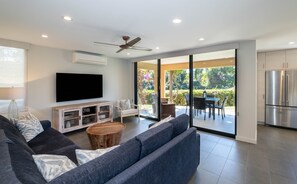 A modern living room with a sofa, TV, and a dining area with chairs and a table.
