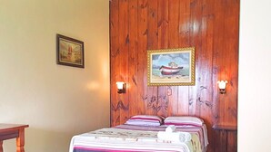 A bedroom with a wooden wall, a bed with striped bedding, two wall-mounted lamps, and a framed picture of a boat.
