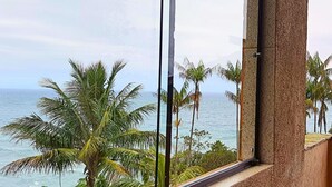 A view from a window overlooking a beach with palm trees and the ocean.
