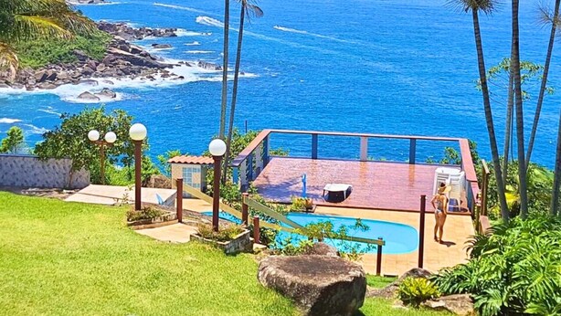 A pool area with a view of the ocean, surrounded by palm trees and a patio with outdoor seating.