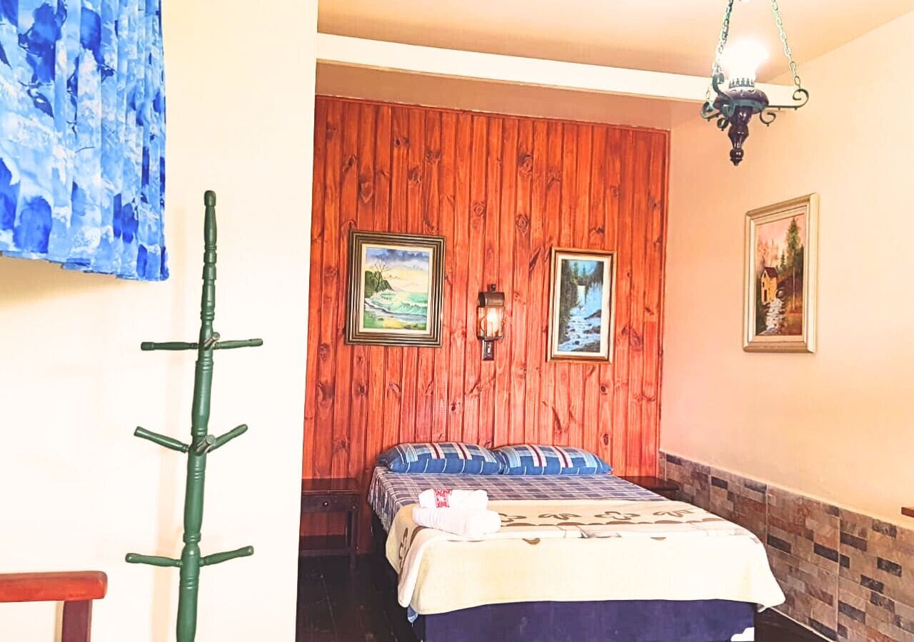 Una habitación con un revestimiento de madera en la pared, una cama con un cojín azul y blanco a rayas y un cuadro en la pared.
