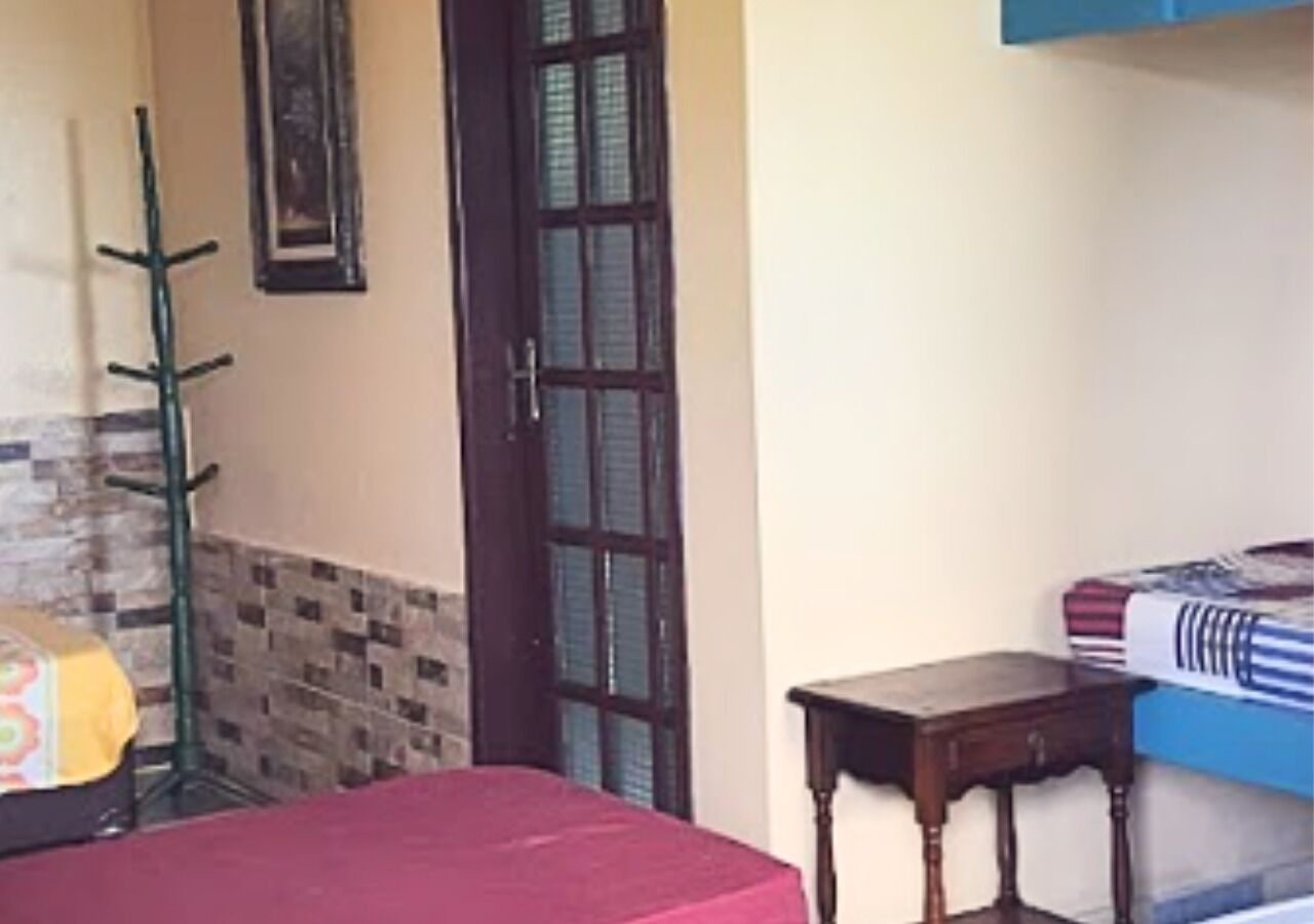 Una habitación con cama, una mesita de madera, un perchero y una puerta con ventana.
