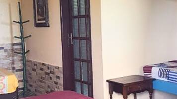 Una habitación con cama, una mesita de madera, un perchero y una puerta con ventana.