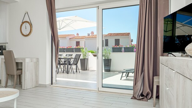 A modern living room with a sliding glass door leading to an outdoor patio, a dining area, and a television on a wooden cabinet. - Villa 'Ada' Independent with Wi-Fi and Air Conditioning (Golfo Aranci)