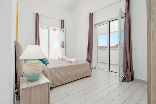 A bedroom with a bed, a lamp, a window, and a sliding door to a balcony.