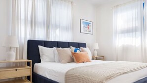 Une chambre à coucher bien rangée, avec une tête de lit bleu foncé, du linge de lit blanc et un plaid tricoté beige.
