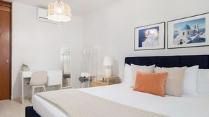 Una habitación de hotel con cama, escritorio, silla, mesita de noche con lámpara y dos cuadros en la pared.