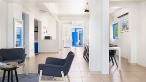 A spacious hallway with a modern design, featuring a seating area with two chairs, a dining table with chairs, and a kitchen area visible in the background.