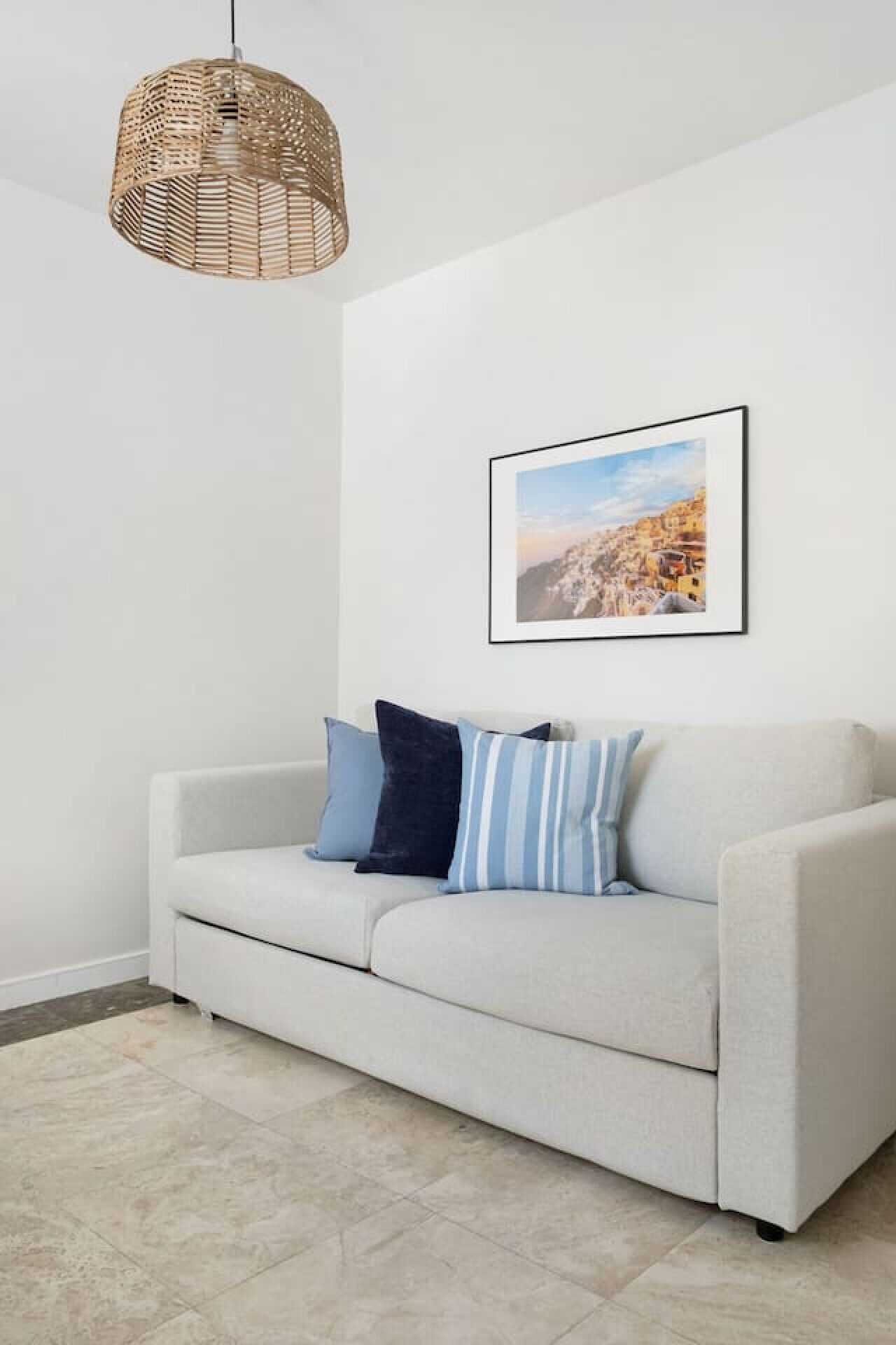 A modern living room with a light grey sofa, a woven pendant light, and a framed landscape painting on the wall.