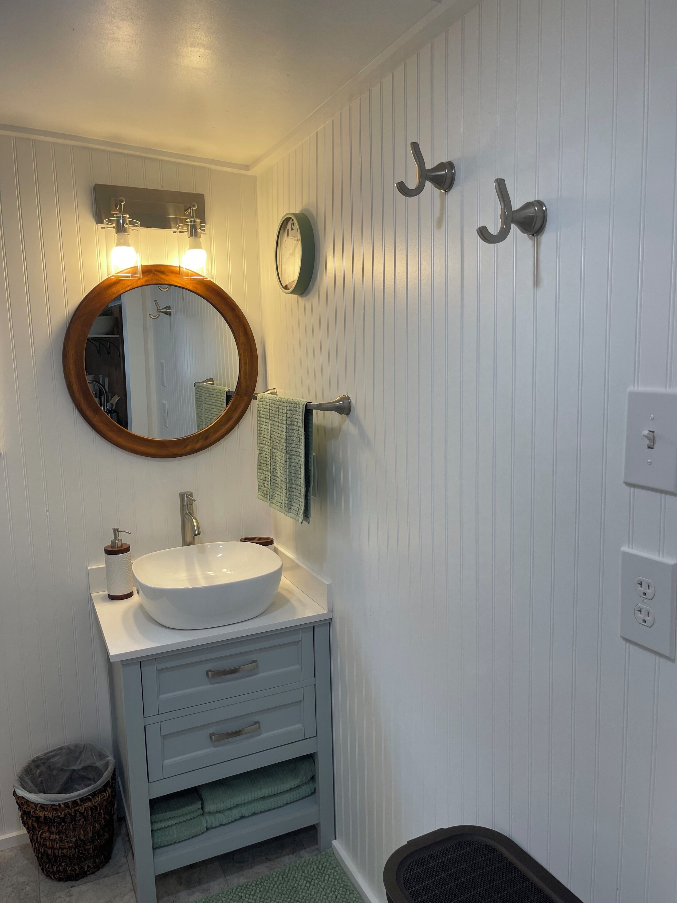 A bathroom with a round mirror, a white sink, a towel rack, and a trash bin.