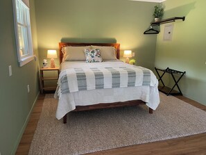 A neatly made bed with a patterned bedspread, two bedside lamps, a wooden nightstand with a tissue box, and a hanging clothes rack.