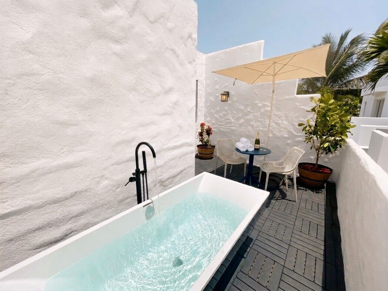 Un espacio de spa con una bañera grande, una pequeña mesa con sillas y una planta en maceta.