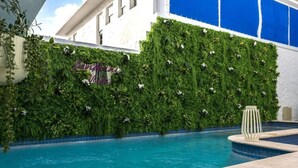 Ein Swimmingpool mit einer vertikalen, grunen Gartenwand und einem dekorativen Schild.