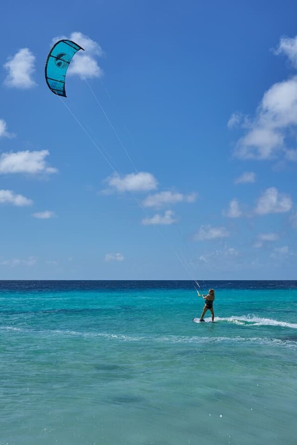 Una persona practicando windsurf en aguas turquesas cristalinas bajo un cielo azul con algunas nubes.