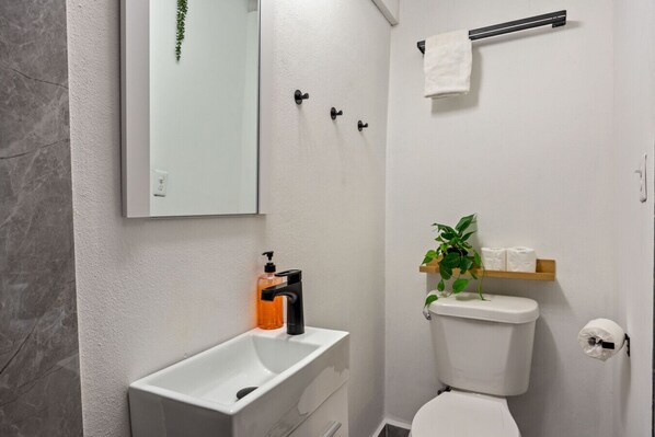 A modern bathroom with a white sink, a toilet, a towel rack, and a small shelf with toiletries.