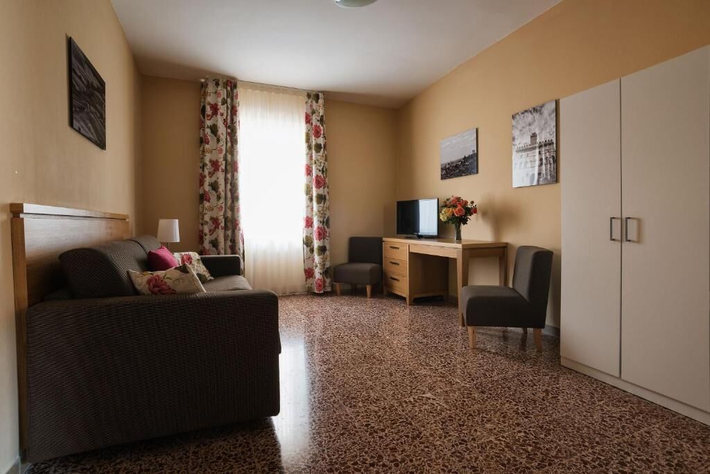 A hotel room with a bed, a desk, a chair, a television, and a wardrobe.