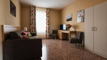 A hotel room with a bed, a desk, a chair, a television, and a wardrobe.