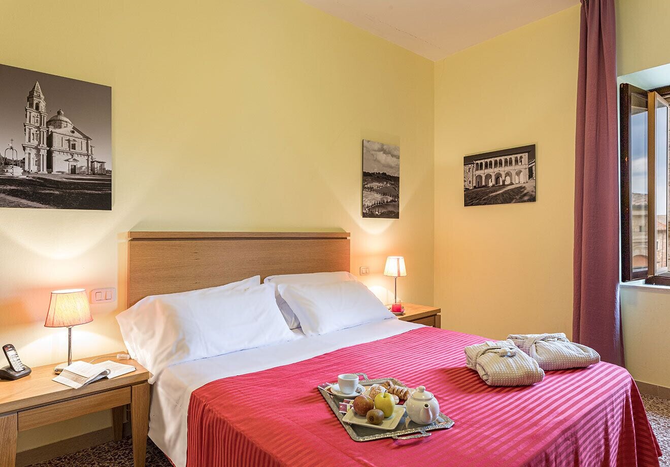 Ein Hotelzimmer mit einem Bett, Nachttischen, einer Lampe, einem Tablett mit Frühstücksangeboten und zwei Bildern an den Wänden.