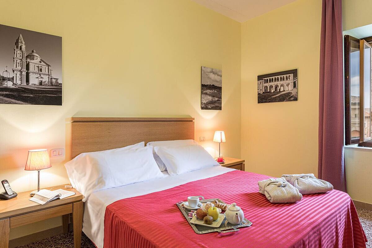 A hotel room with a bed, bedside tables, a lamp, a tray with breakfast items, and two paintings on the walls.