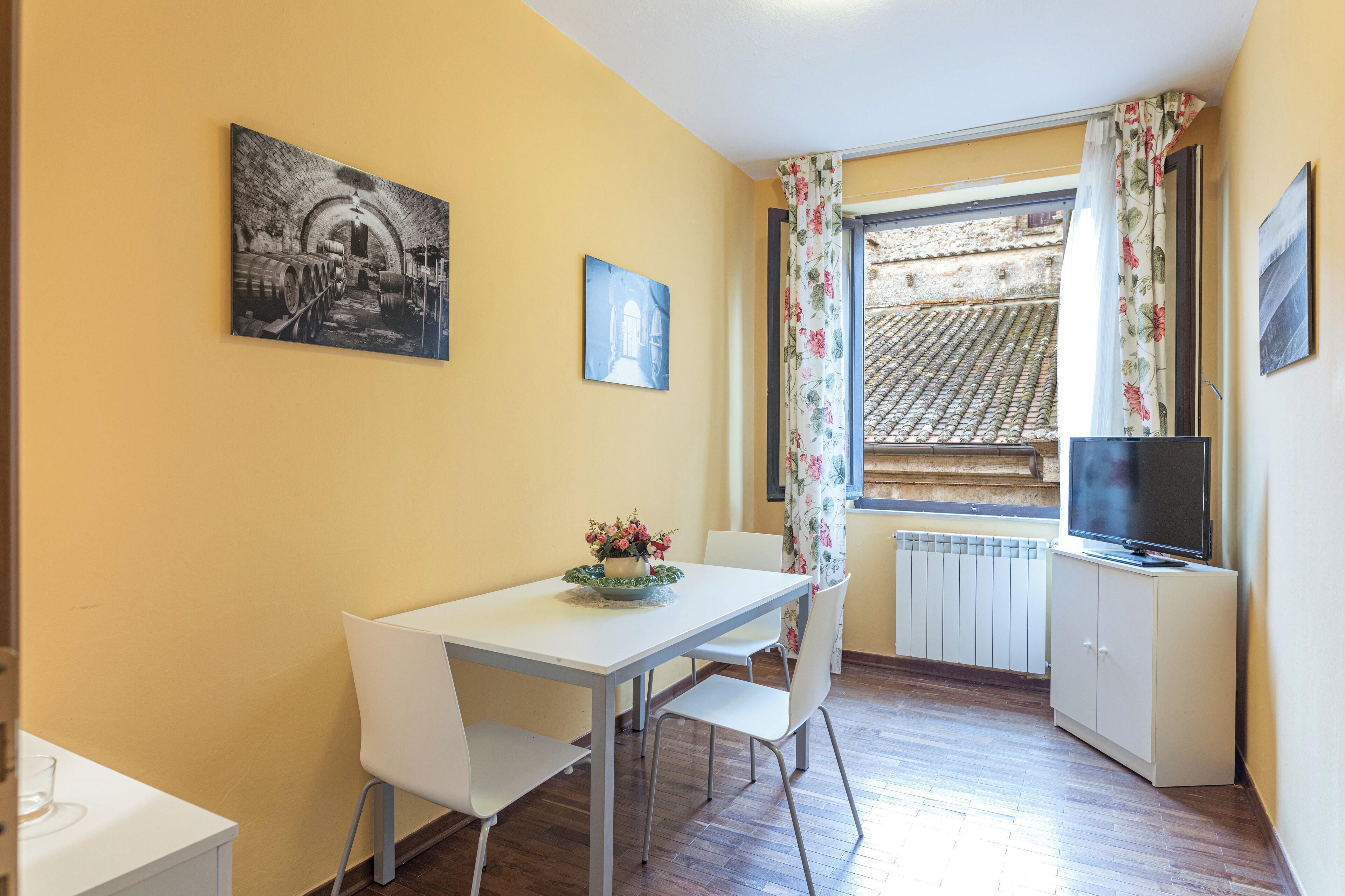 A dining area with a table, chairs, a TV, and a window with curtains.