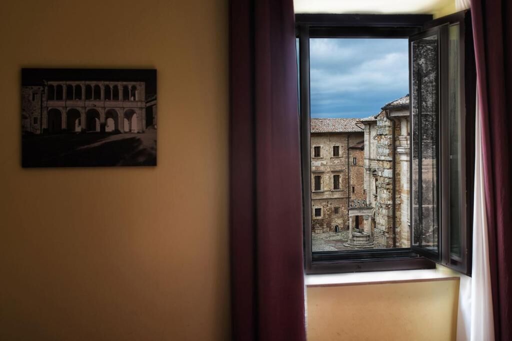 A room with a window overlooking an old building with arches.